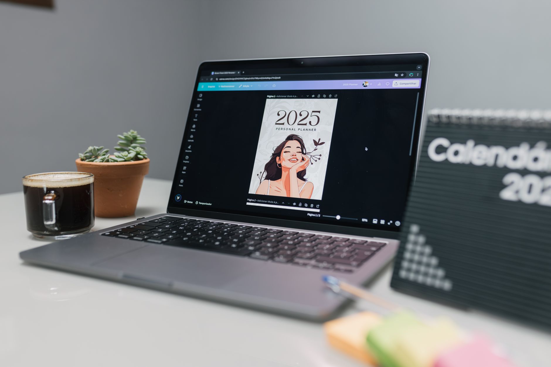 A laptop on a clean white desk displaying a colorful digital planner template next to a notebook and coffee mug.